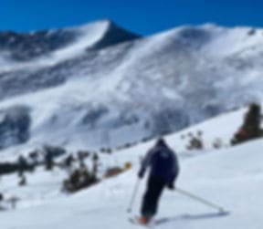A skier pausing on an open slope facing a wind-scoured summit