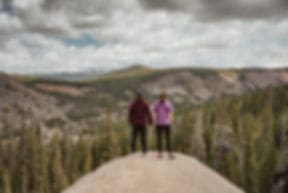 Two hikers standing on a rock outcrop looking out over forested valleys